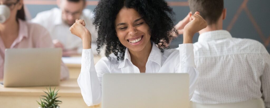 Tips Performance Appraisals; Image shows a woman sitting in an office space being happy & seeming to celebrate an achievement